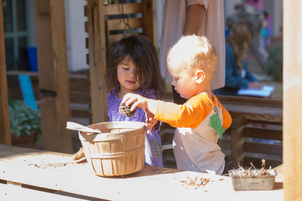 Older Toddlers play in the outdoor classroom kitchen hut