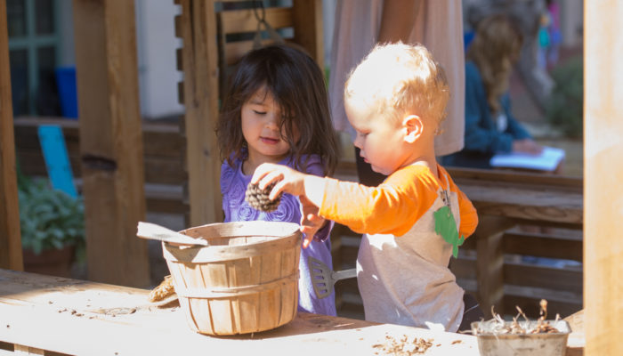 Older Toddlers play in the outdoor classroom kitchen hut